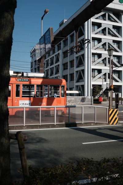 白天，白色大楼附近的道路上有红白相间的公共汽车